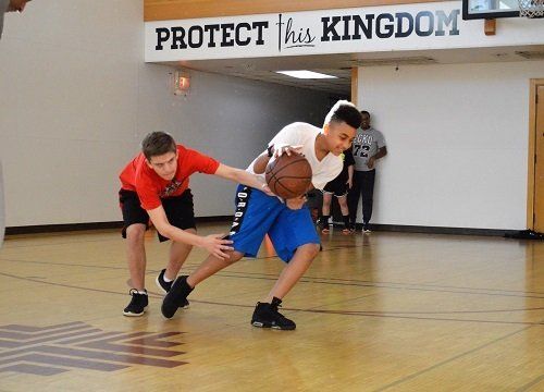 Two boys are playing basketball in front of a sign that says protect his kingdom