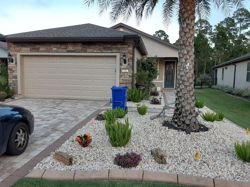 A car is parked in front of a house with a blue trash can.