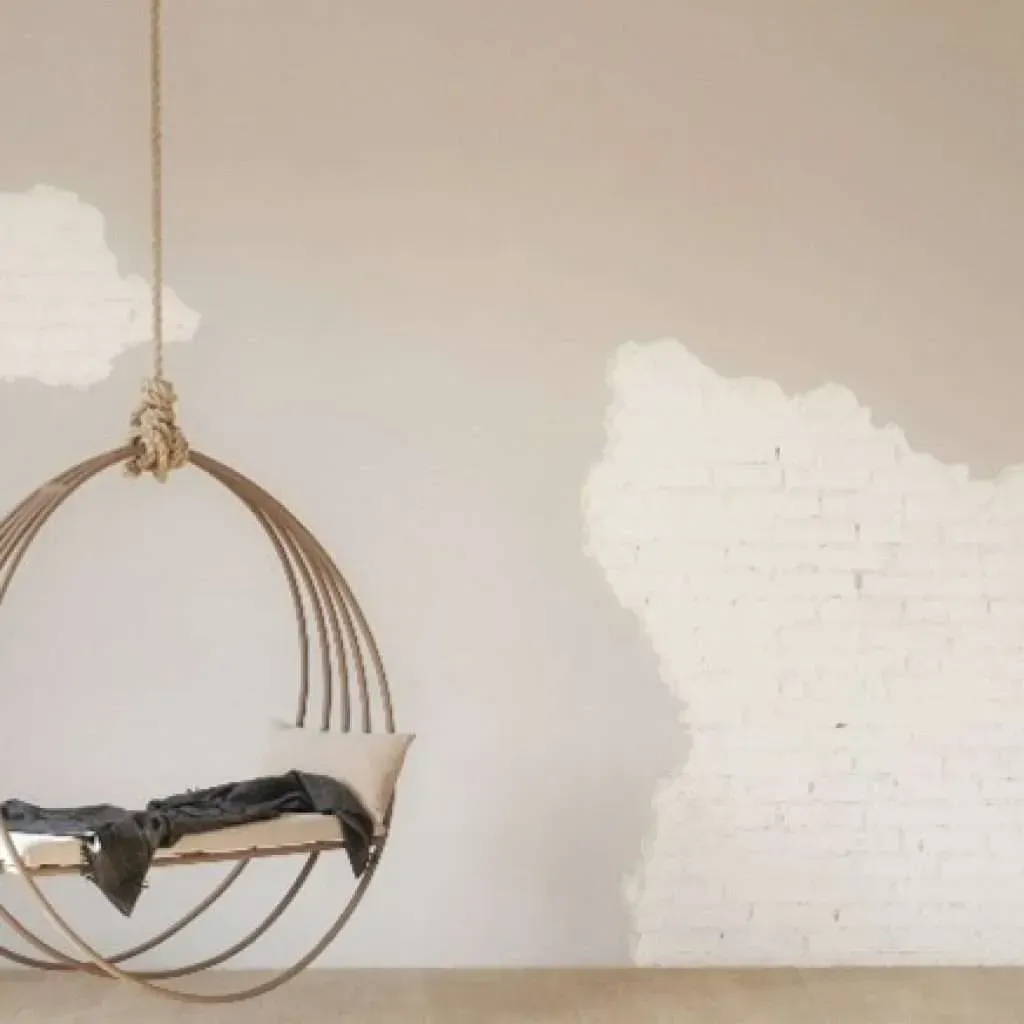 Hanging metal chair with blanket and pillow, on a neutral wall.