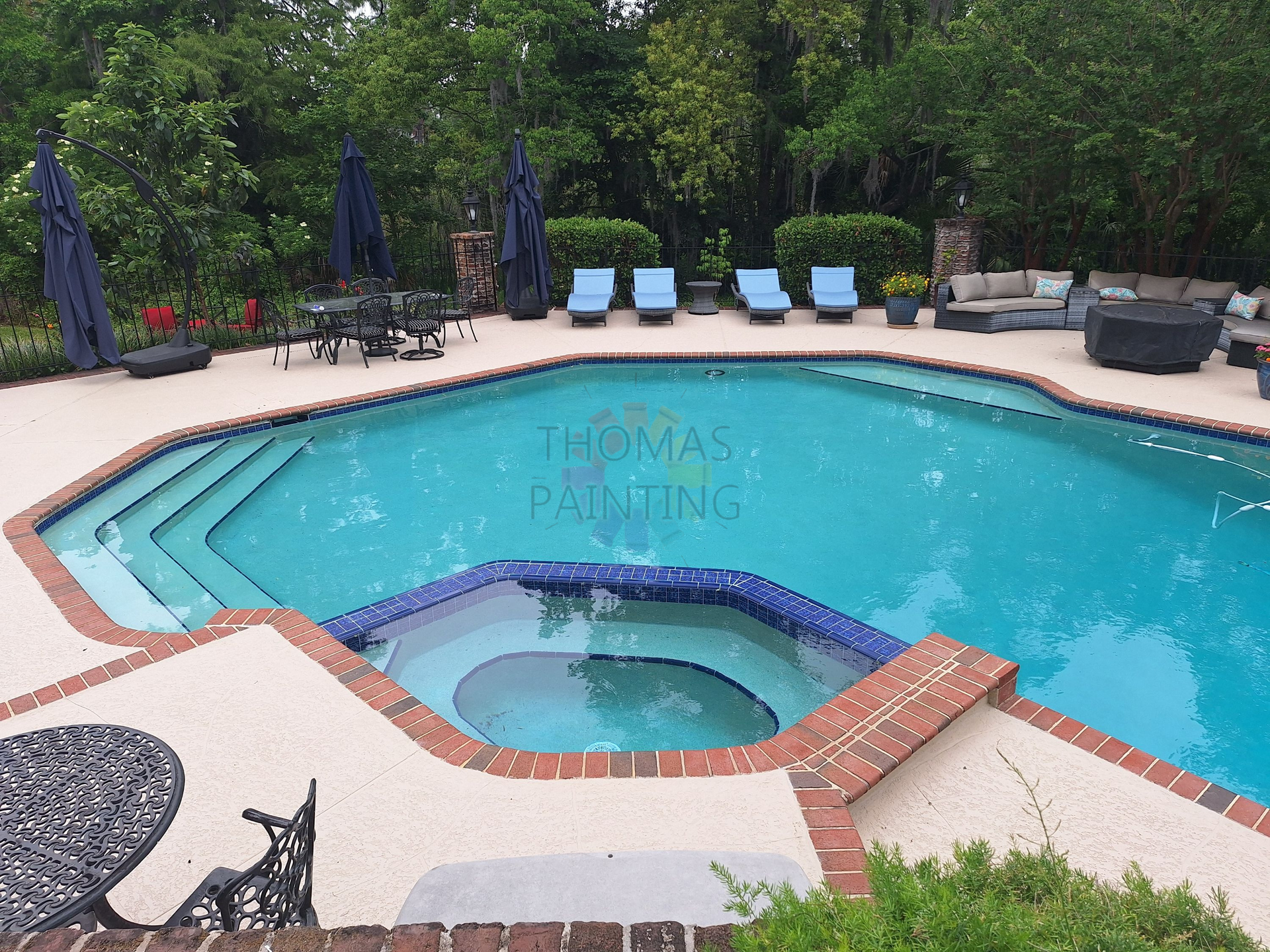 Backyard swimming pool with hot tub, blue lounge chairs, and patio seating surrounded by trees