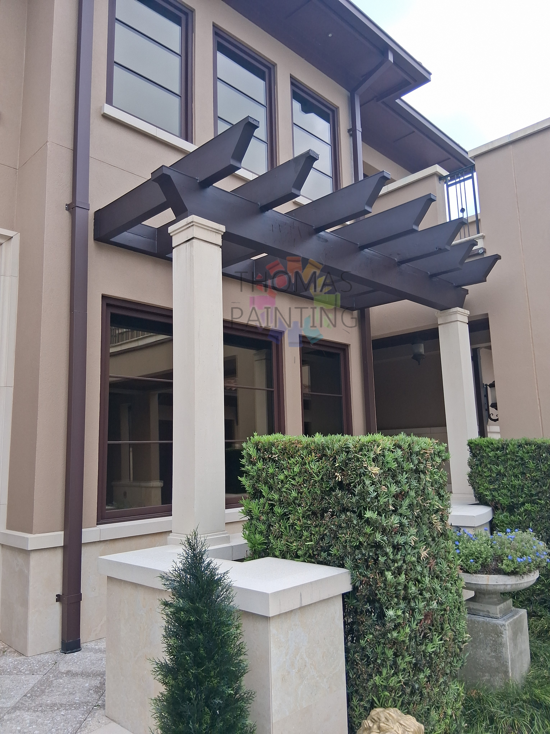 Modern two-story house with cream columns, dark pergola, and trimmed hedges by the entrance