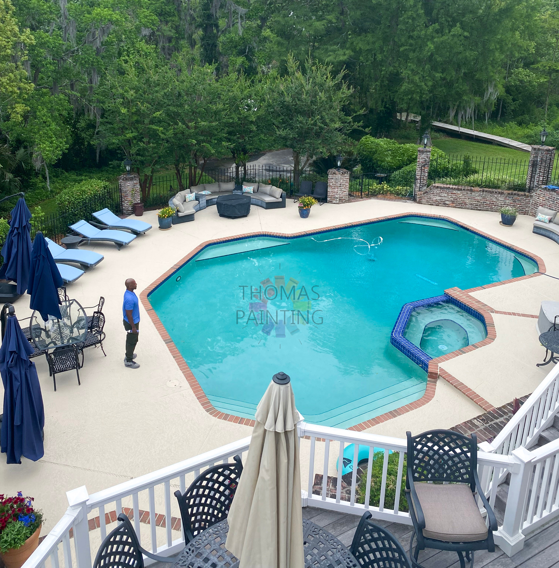 Outdoor swimming pool with lounge chairs, umbrellas, and a hot tub surrounded by trees