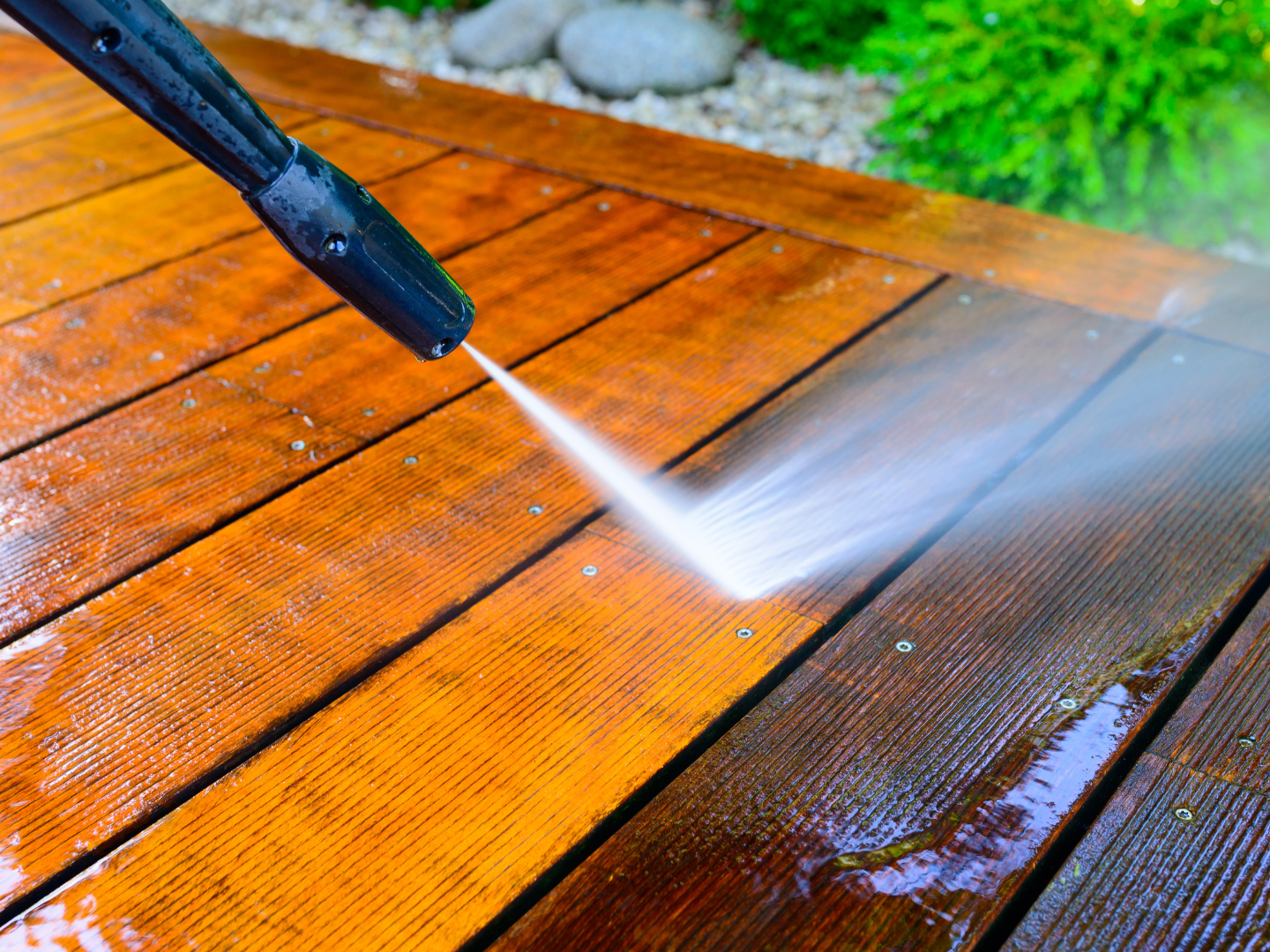 A person is using a high pressure washer to clean a wooden deck.