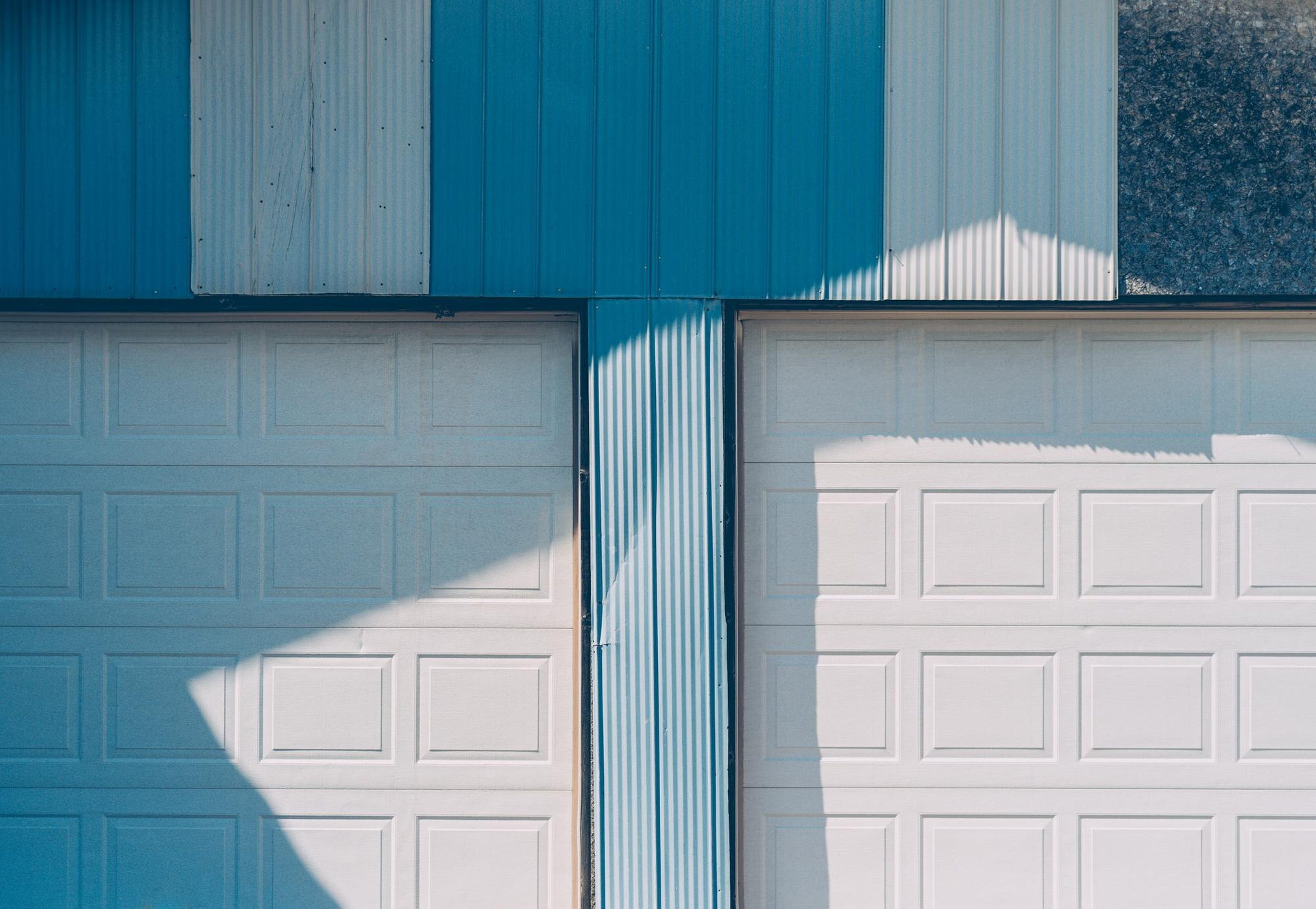 Blue and white garage doors with sharp sunlight and shadows on a corrugated metal wall