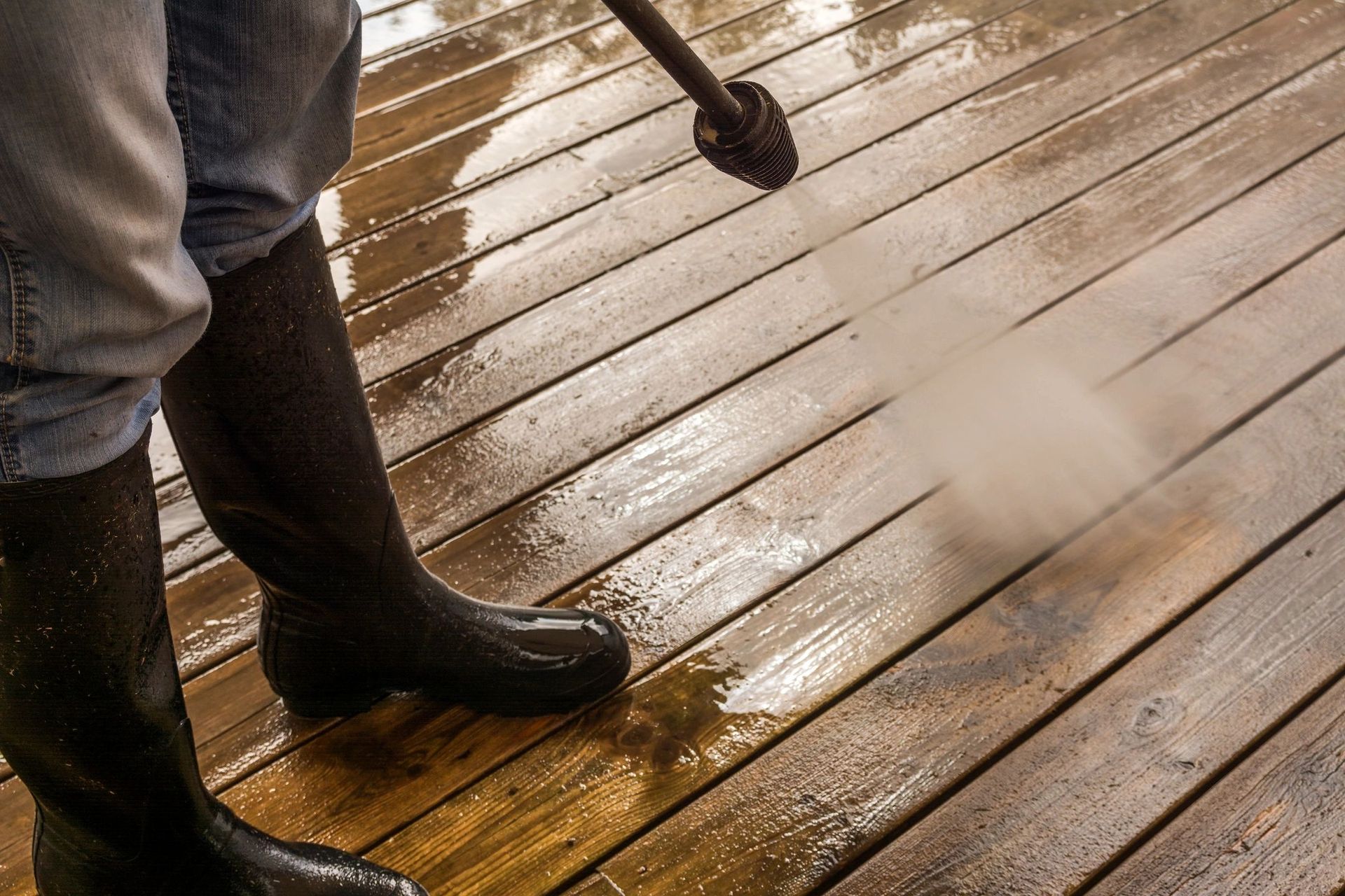 A person is cleaning a wooden deck with a high pressure washer.
