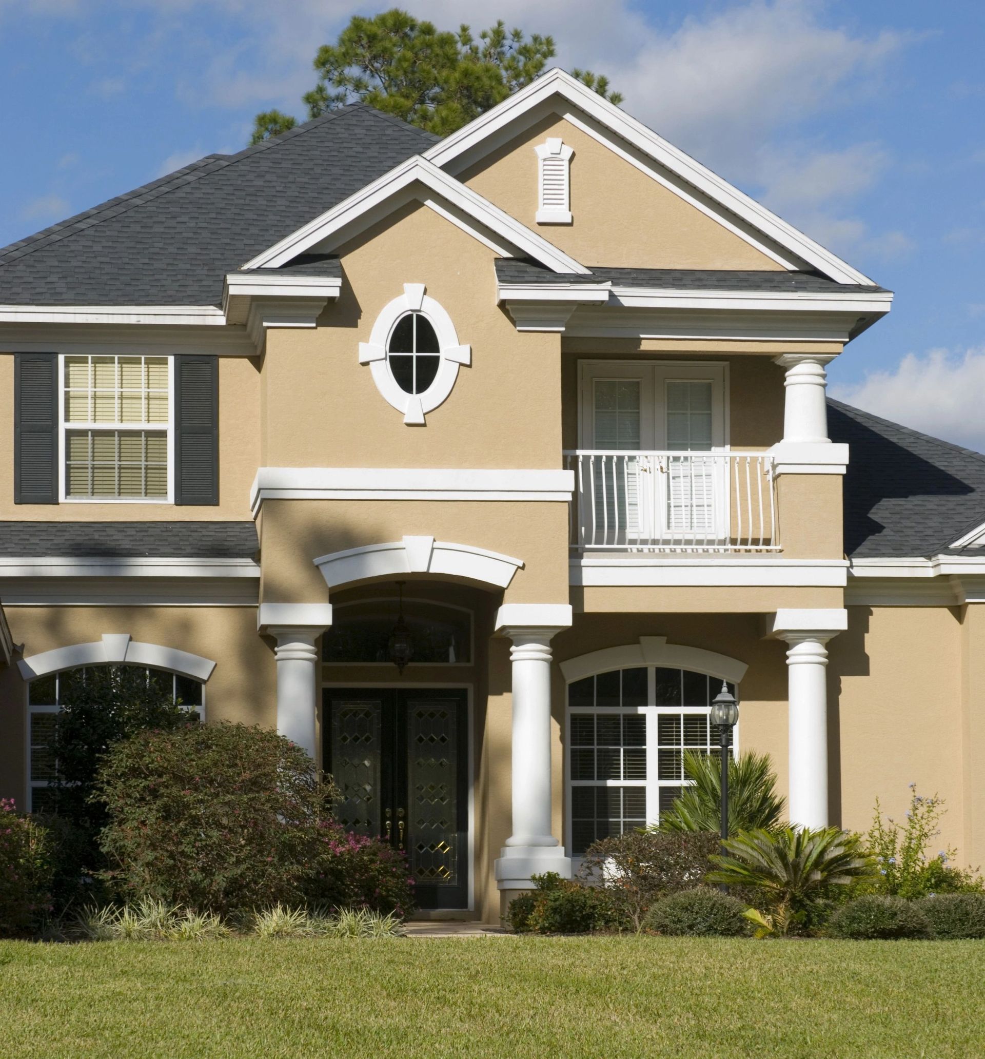 A large tan house with black shutters and a balcony