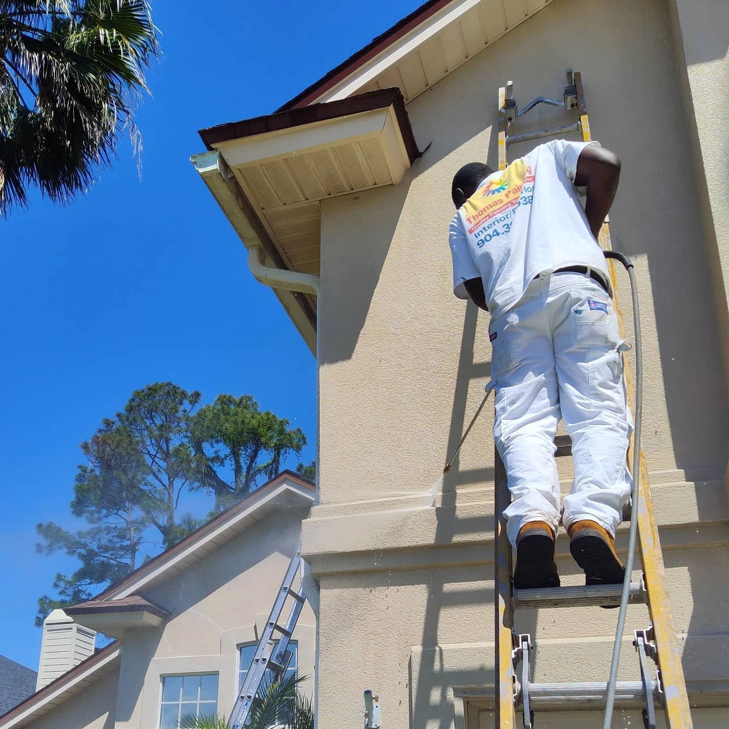A man is standing on a ladder painting a house