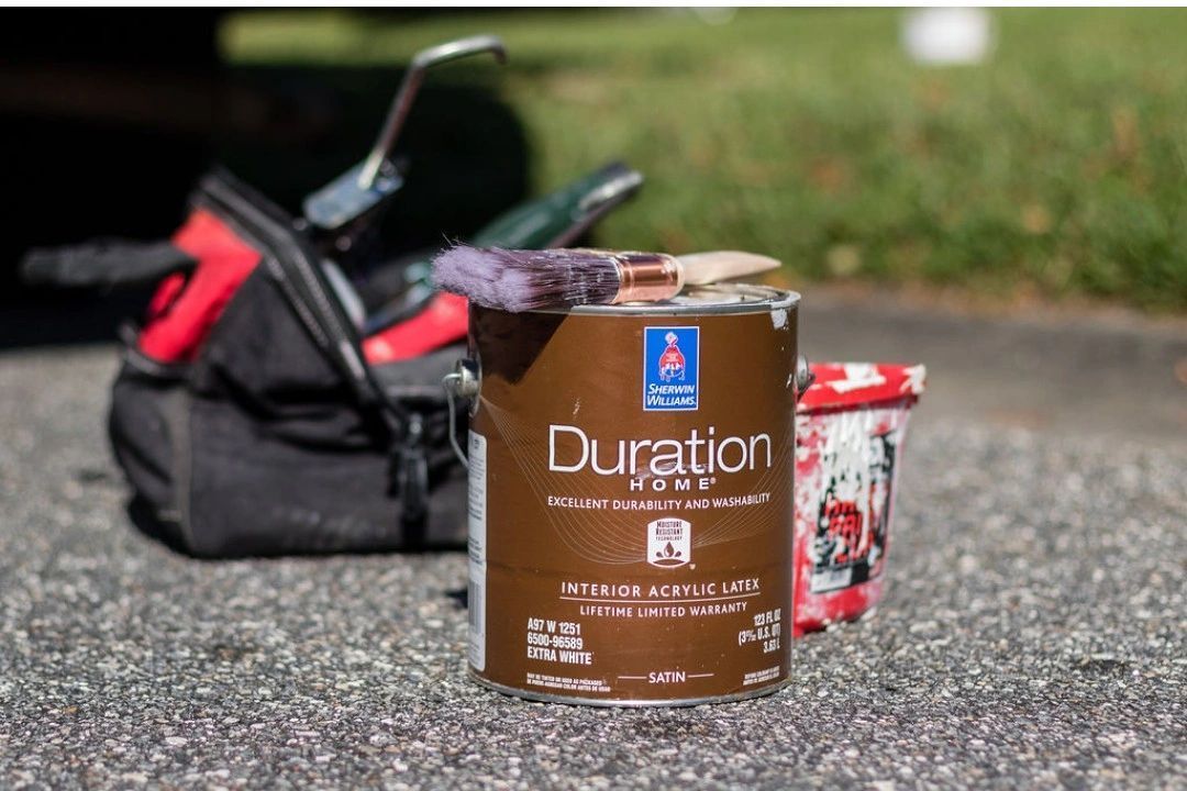 A can of duration paint is sitting on the ground next to a tool bag.