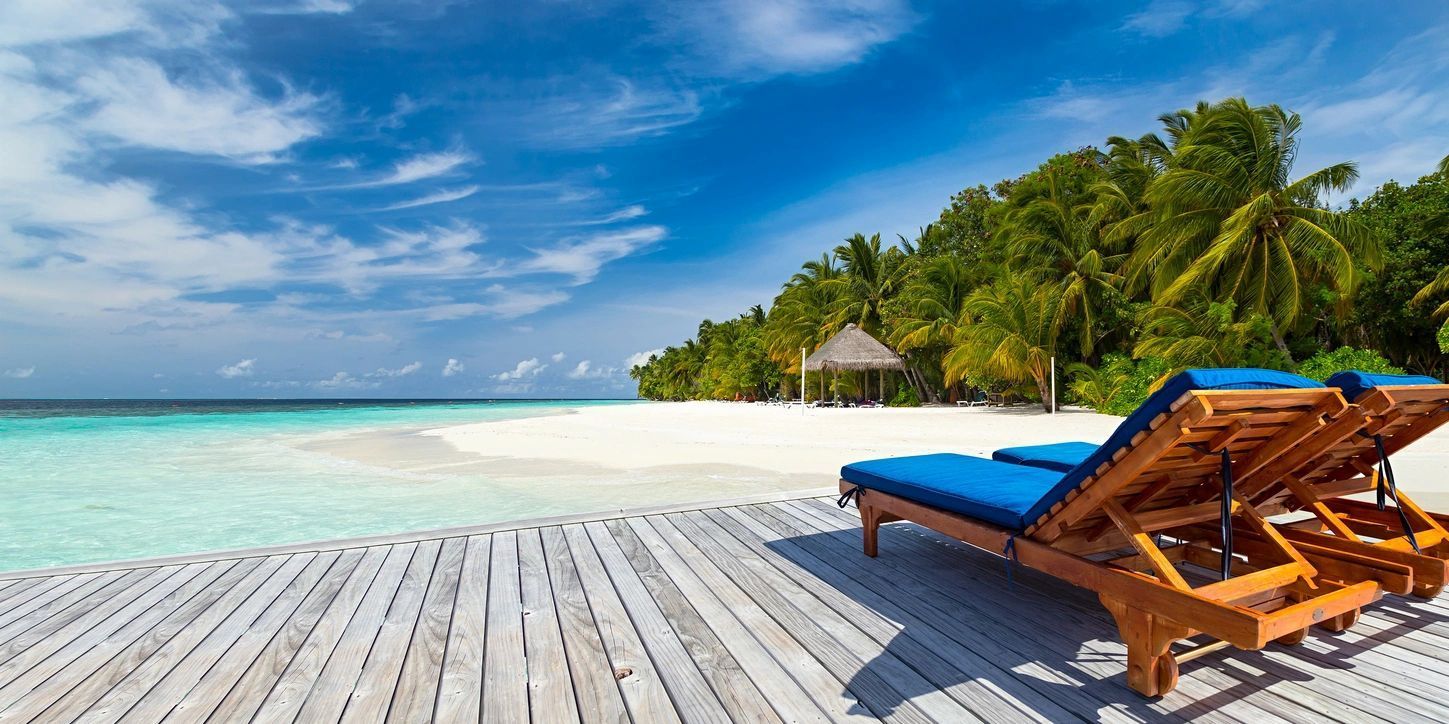 Two lounge chairs are sitting on a wooden deck on a tropical beach.