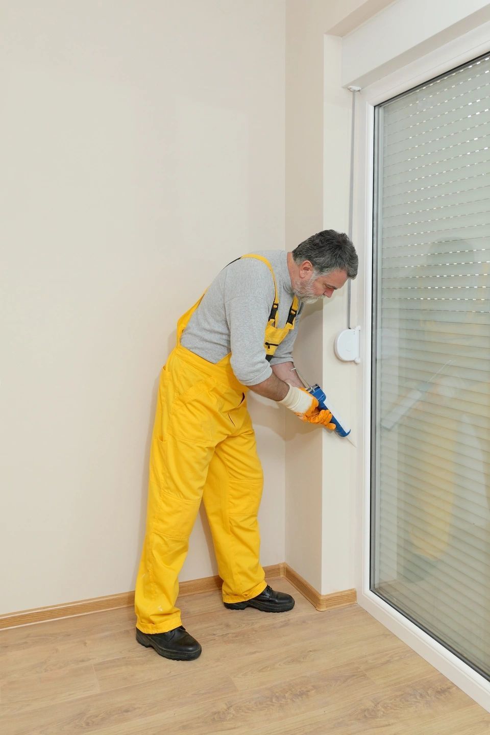 A man in yellow overalls is cleaning a window with a broom.