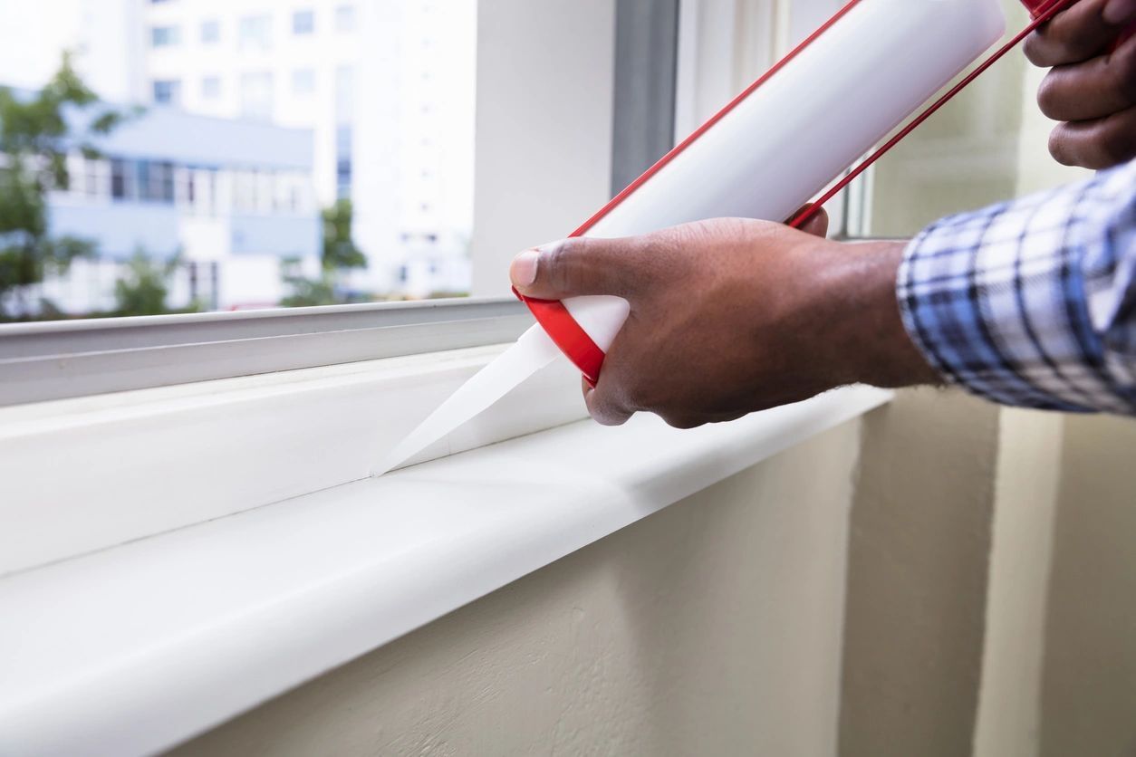 A man is applying sealant to a window sill.