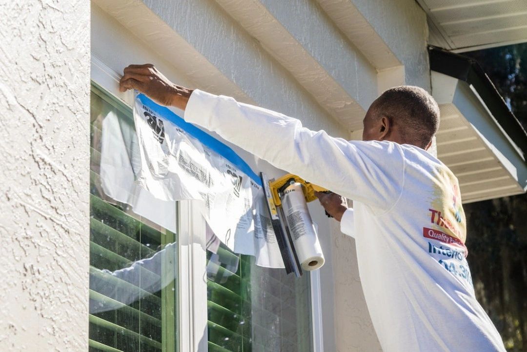 A man is painting a window with blue tape.