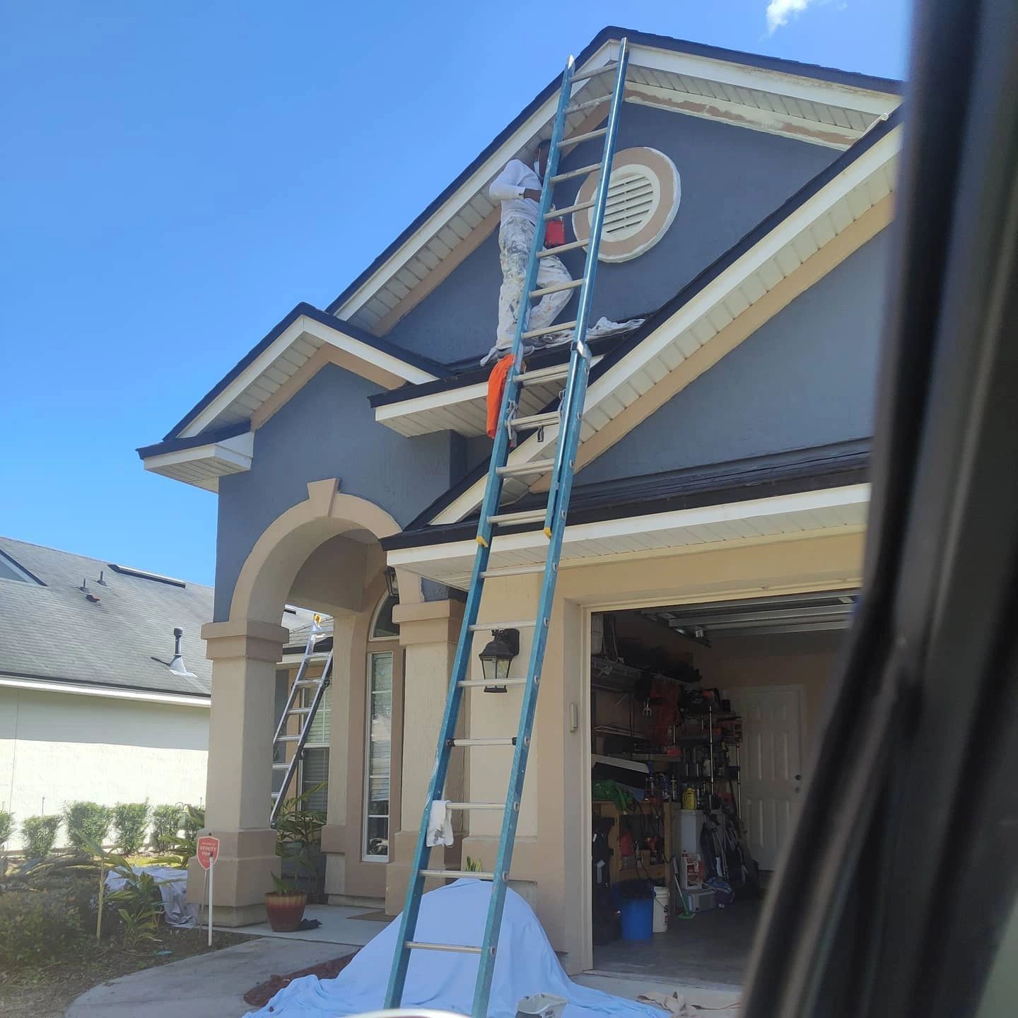 A man on a ladder paints the side of a house