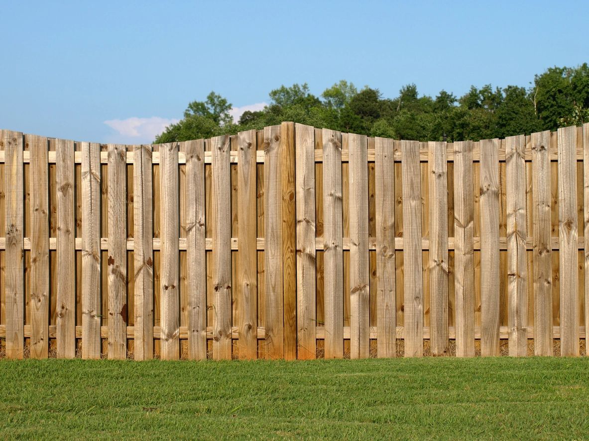 A wooden fence is in the middle of a lush green field.