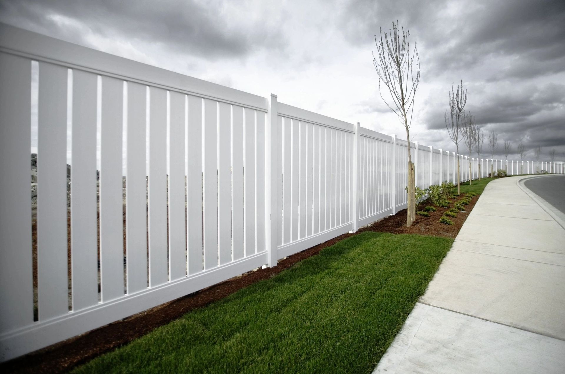 A white fence along a sidewalk with a cloudy sky in the background.