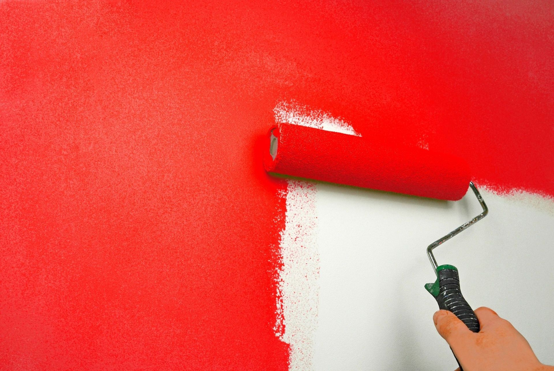 A person is painting a wall red and white with a paint roller.