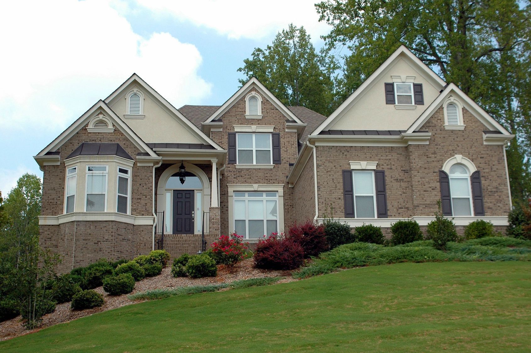 A large brick house sits on top of a lush green hillside