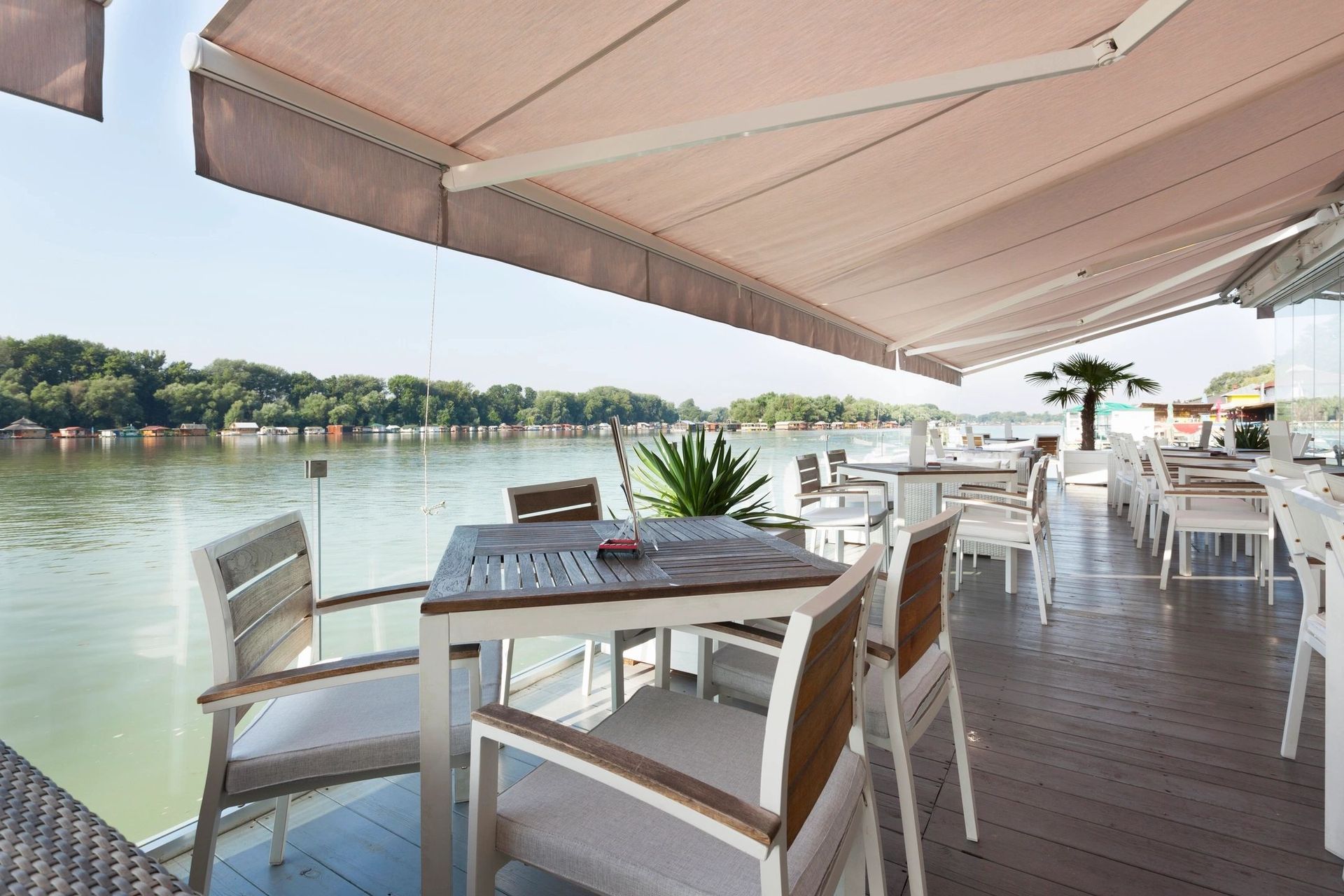 A restaurant with tables and chairs under an awning overlooking a body of water.