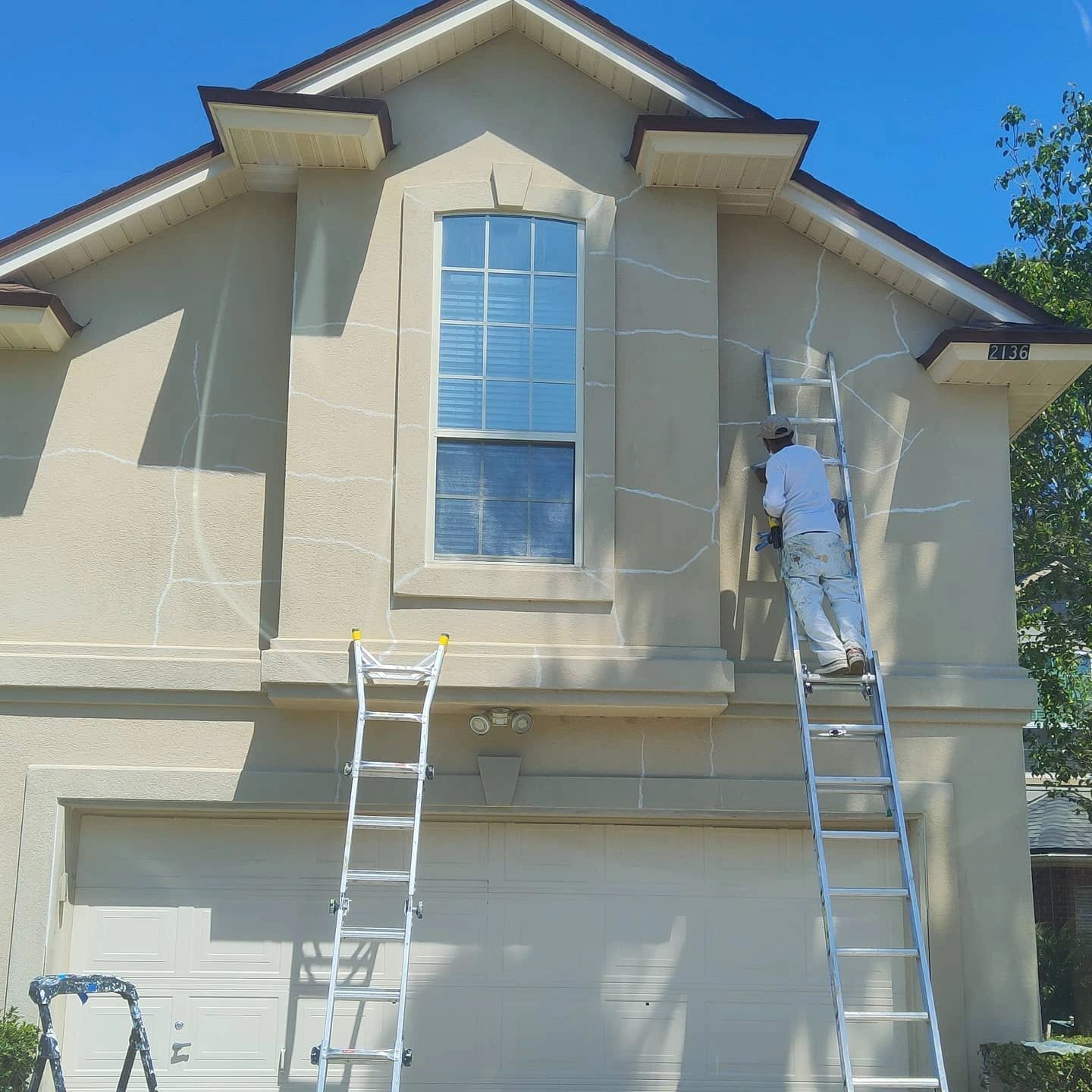 A man on a ladder paints the outside of a house