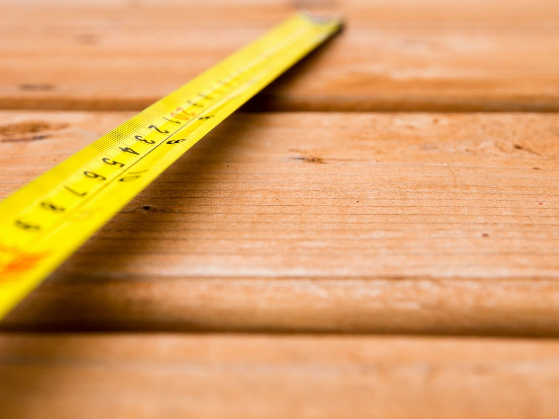 A yellow tape measure is sitting on a wooden table.