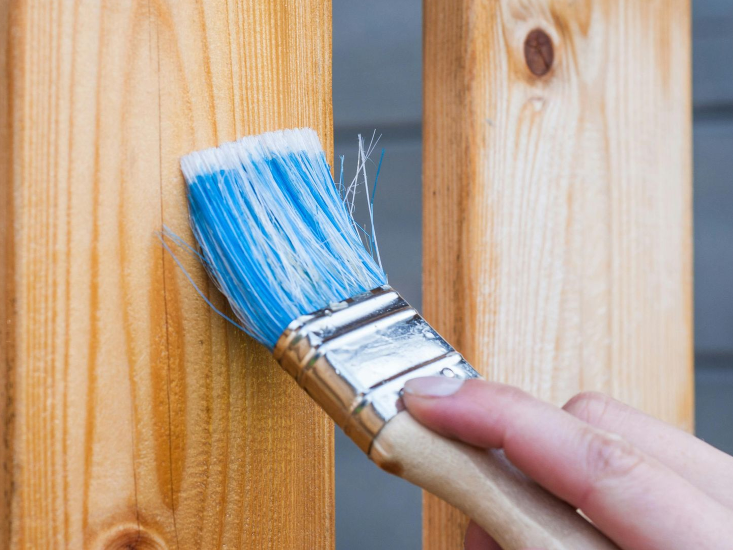 A person is using a high pressure washer to clean a wooden deck.