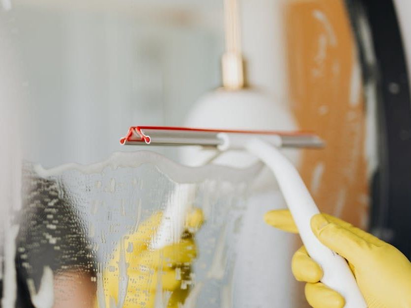 A person wearing yellow gloves is cleaning a window with a squeegee.