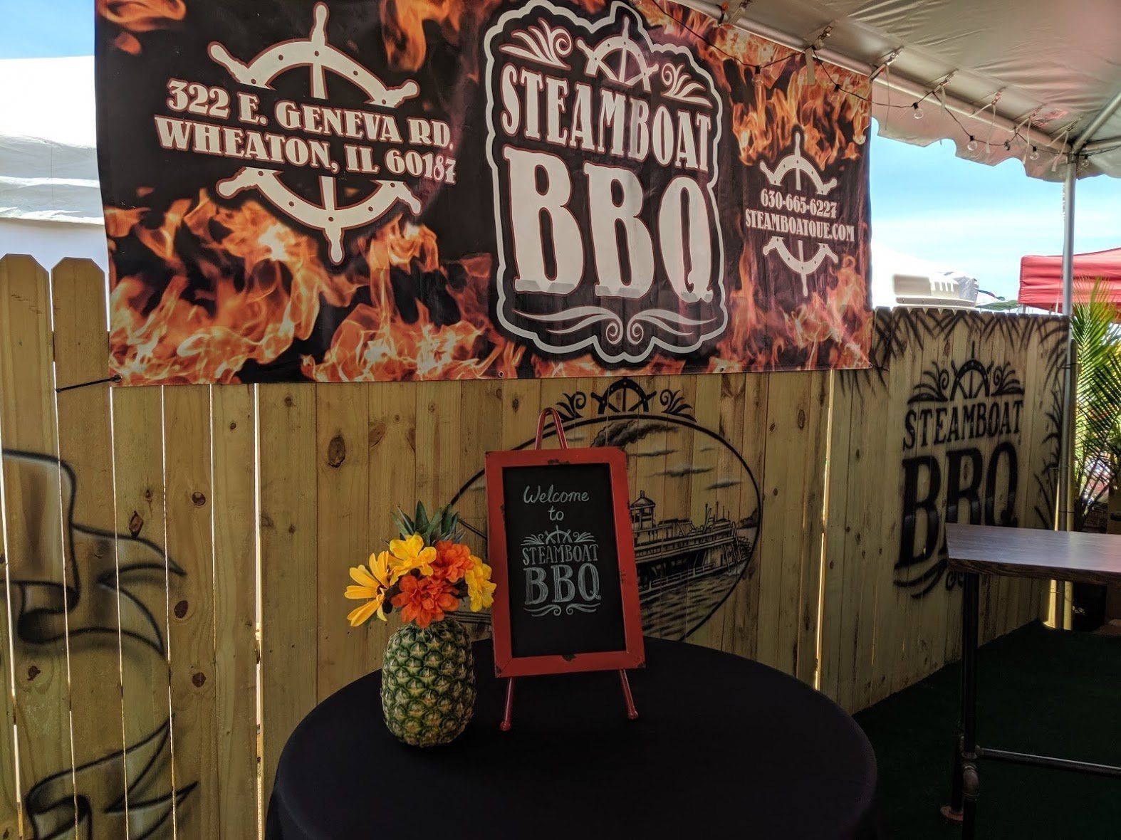 A sign for steamboat bbq is behind a wooden fence