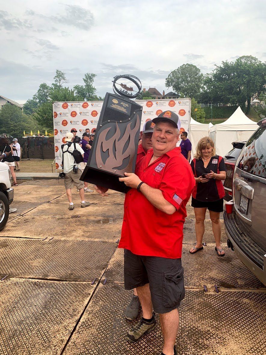 A man in a red shirt is holding a trophy in a parking lot