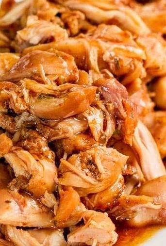 A close up of a plate of shredded chicken with sauce on a table.