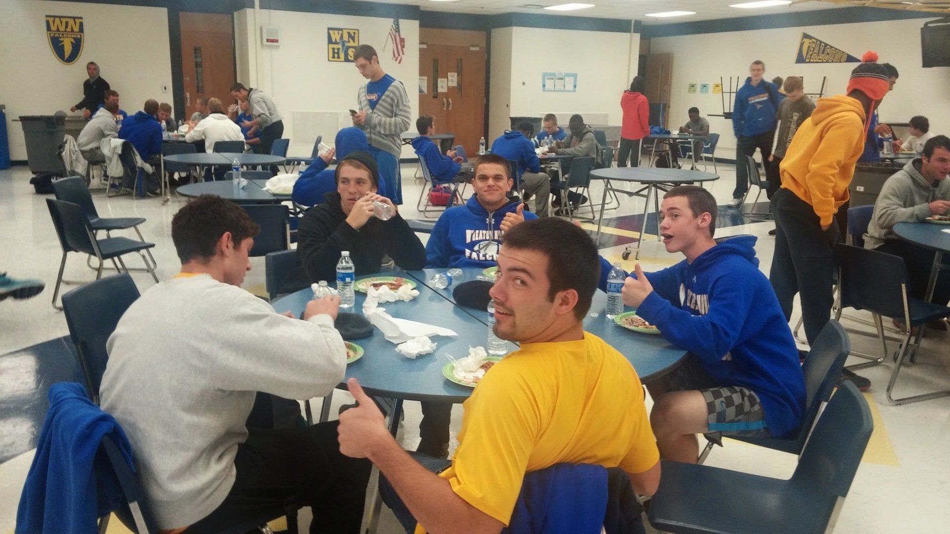 A group of young men are sitting at tables in a cafeteria eating food
