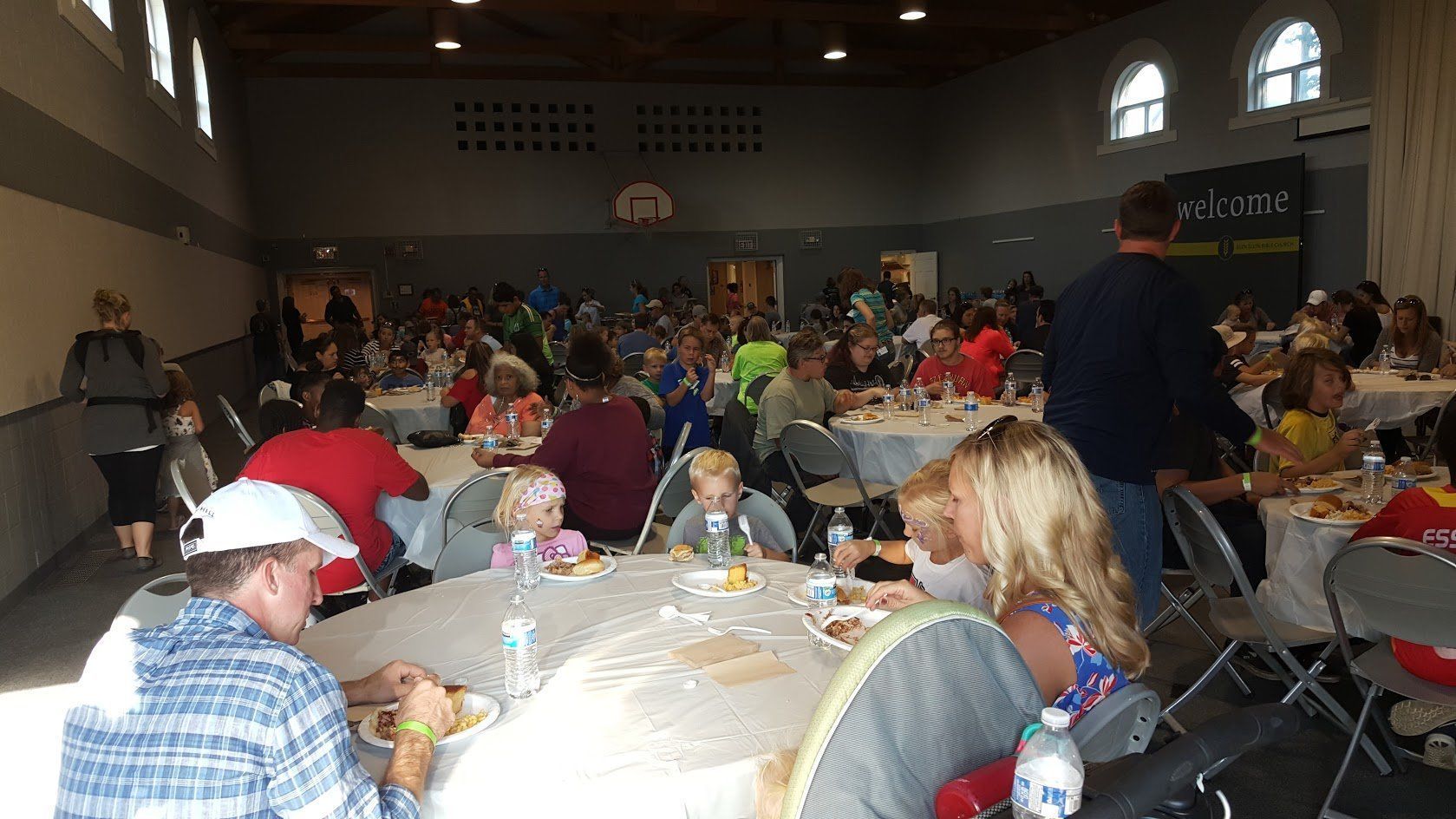 A large group of people are sitting at tables in a large room eating food.
