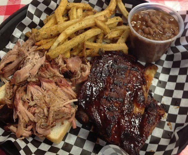 A plate of pulled pork , ribs , french fries and beans on a checkered napkin.