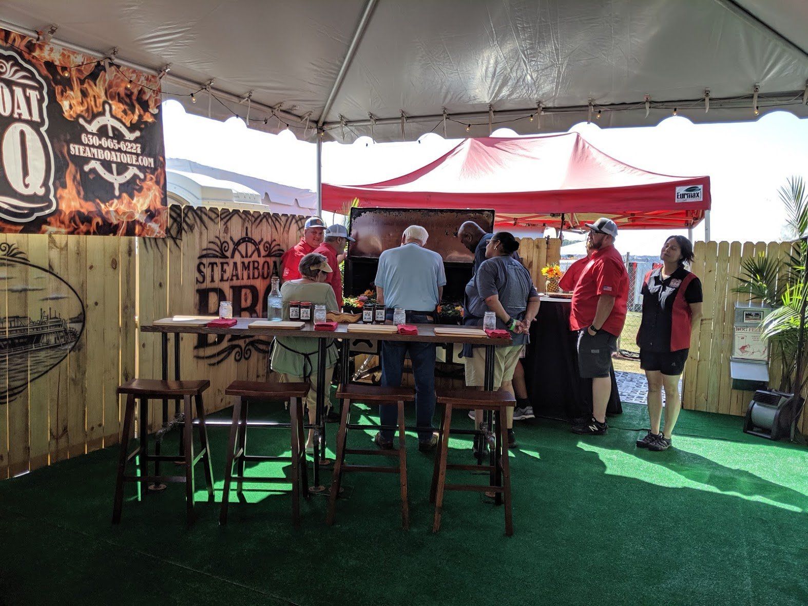 A group of people are standing around tables under a tent.