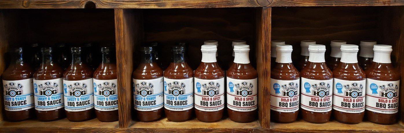 A row of bottles of hot sauce are lined up on a wooden shelf.
