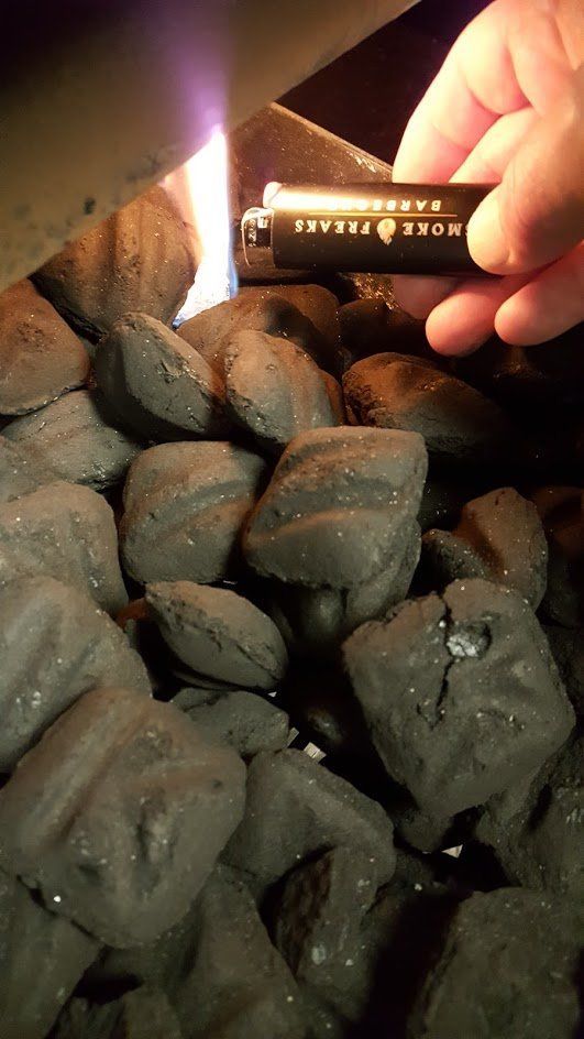 A person is holding a lighter over a pile of coals.