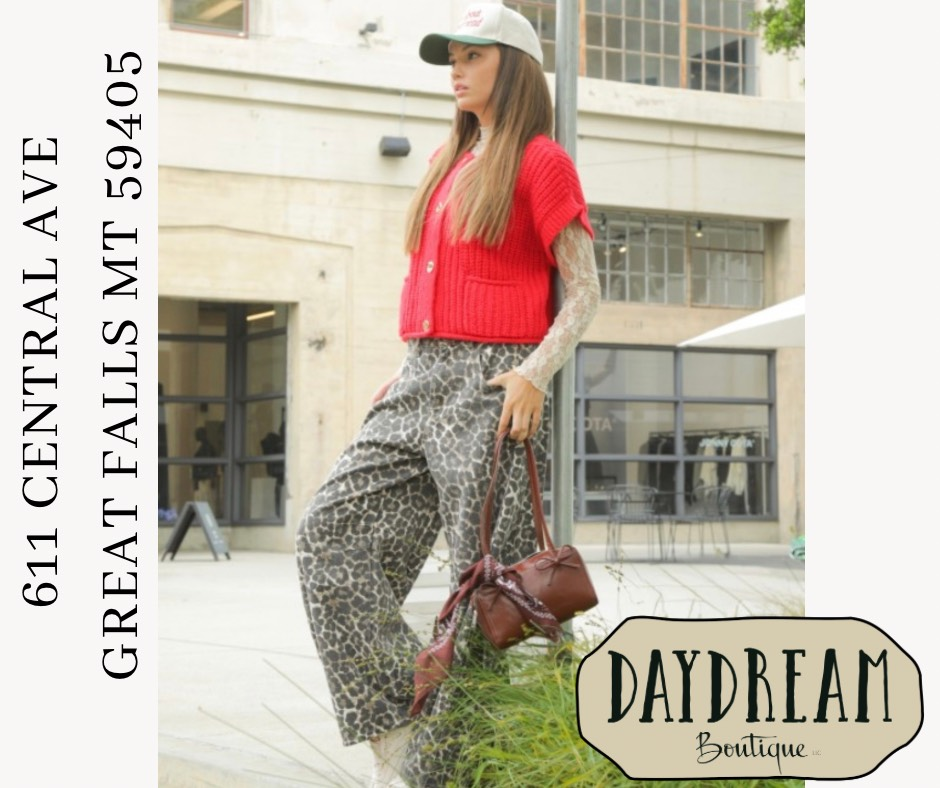 Woman in red top, patterned pants, holding a purse outside a boutique in Great Falls, MT.