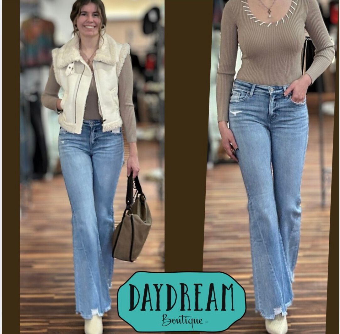 Two women modeling jeans and tops in a boutique setting, one with a vest, both smiling.