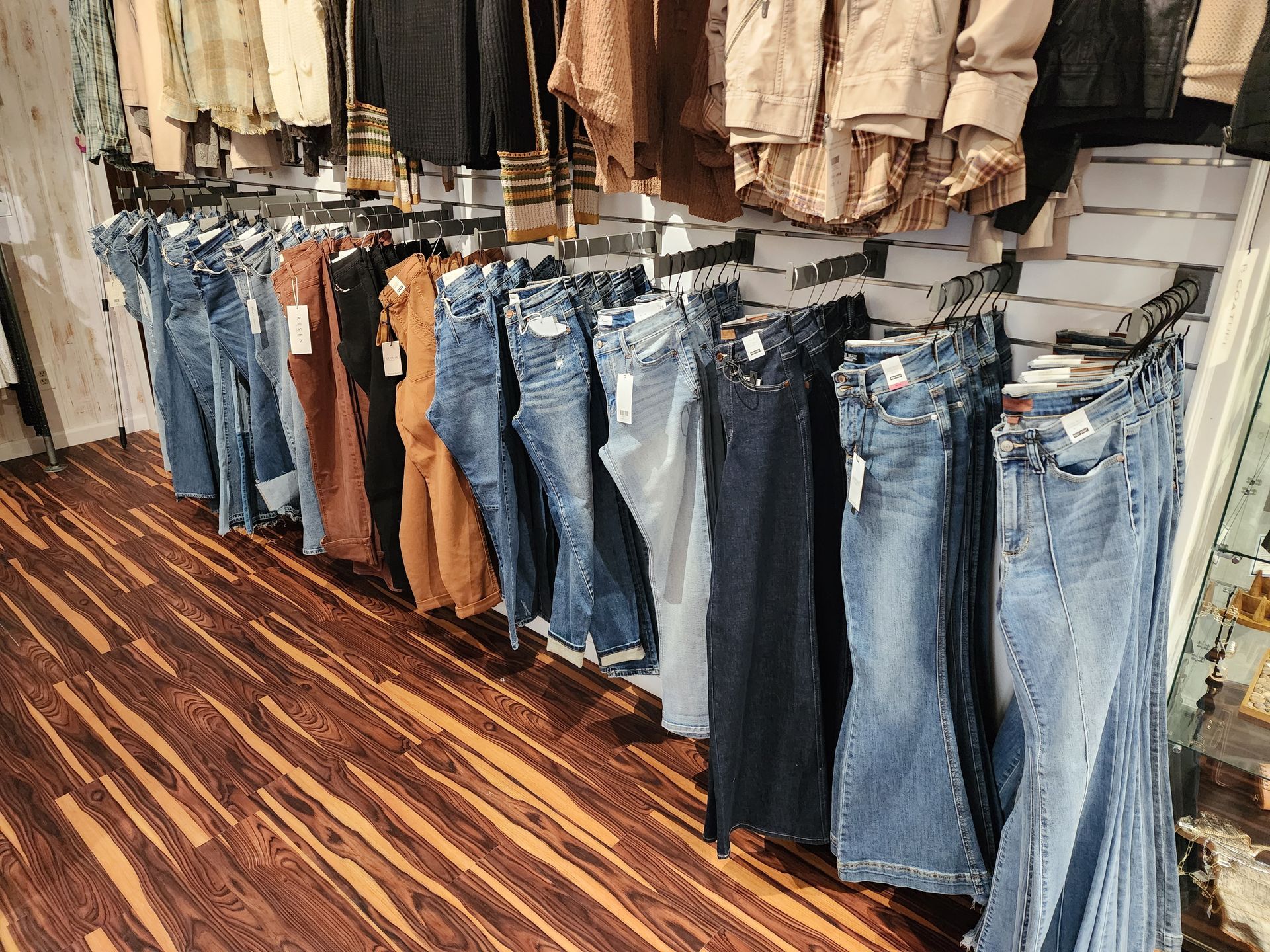Row of jeans hanging in a clothing store, with shirts above.