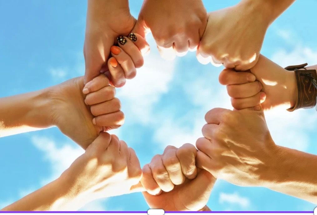 Eight hands joined together in a circle, holding fists, against a blue sky.