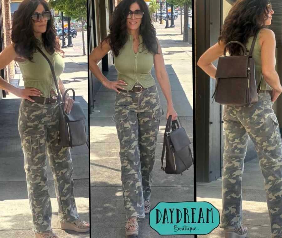 Woman wearing olive top, camouflage pants, and carrying a purse and backpack outdoors.