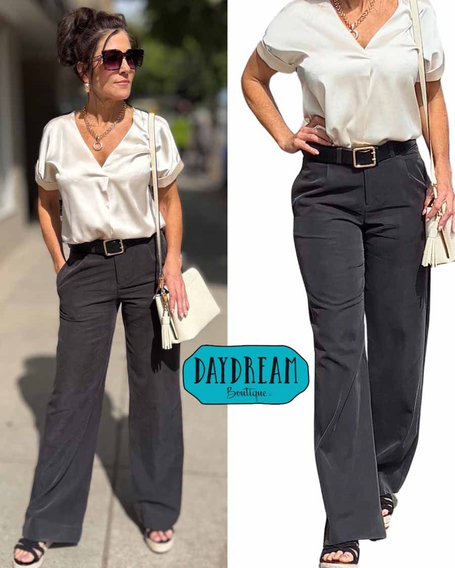 Woman in ivory blouse and black pants, smiling, with purse, sunglasses.