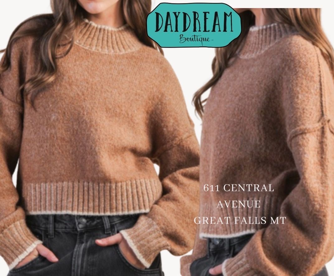 Woman wearing a brown sweater with white trim, standing in front of the Daydream Boutique store.