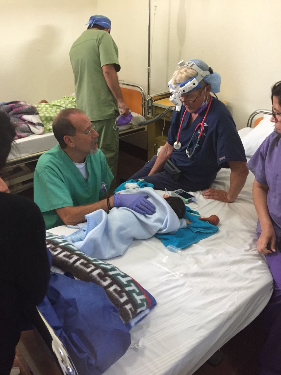 Ein Ärzteteam kümmert sich in einem Krankenhauszimmer um ein neugeborenes, blau gewickeltes Baby.