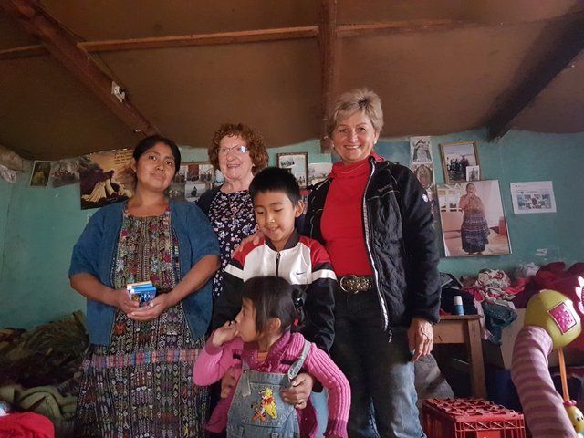 Eine Gruppe lächelnder Menschen in einem geschlossenen Raum; zwei Frauen und zwei Kinder, unordentliches Zimmer.