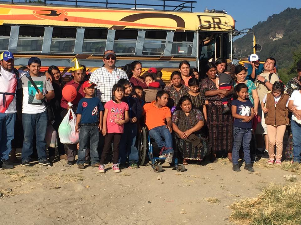 Eine Gruppe von Menschen posiert vor einem gelben Bus in einem Berggebiet.