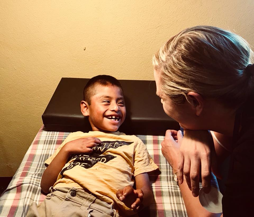 Ein Junge mit breitem Lächeln liegt da und schaut eine Frau an, die sich zu ihm beugt; 