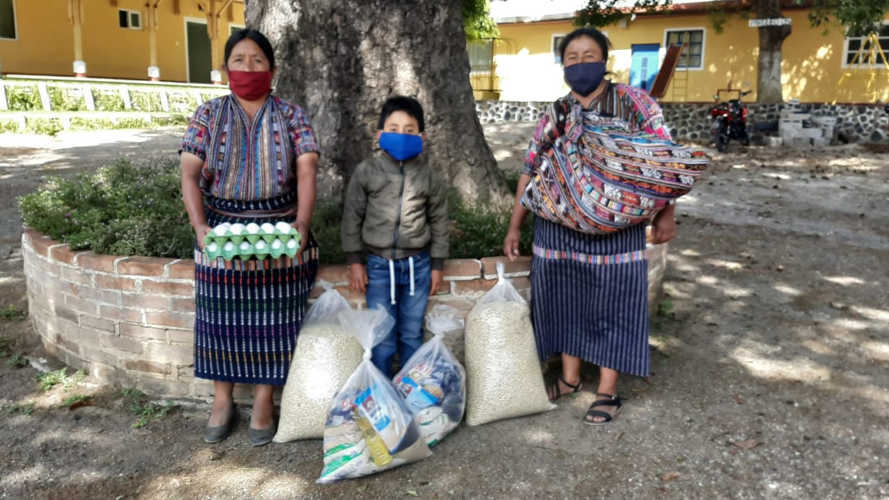 Drei Personen mit Vorräten: Eier und Tüten mit Lebensmitteln. Im Freien in der Nähe eines Gebäudes und eines Baumes, 
