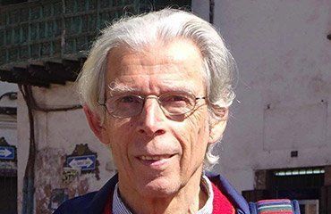 Ein Mann mit grauen Haaren und Brille lächelt im Freien.