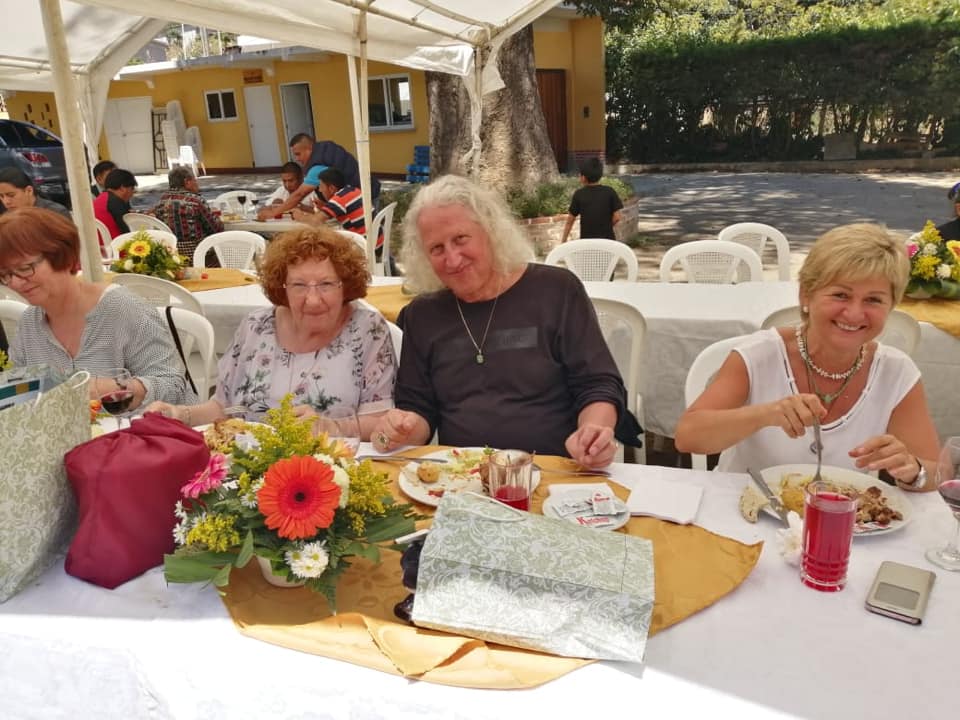 Menschen sitzen im Freien an einem gedeckten Tisch, möglicherweise eine Feier. 