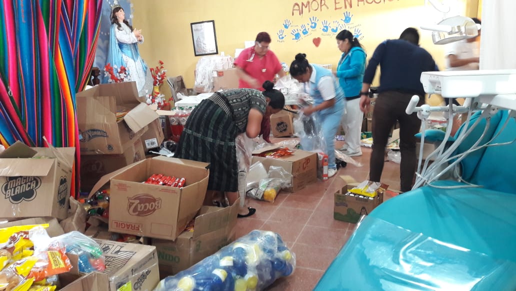 Menschen sortieren in einem Raum Kisten mit Hilfsgütern, einige tragen medizinische OP-Kleidung.